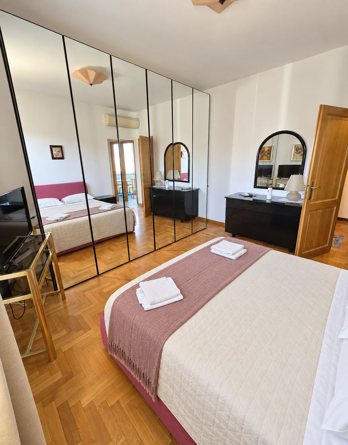A hotel room with a bed, a desk, a dresser, a mirror, and a television.