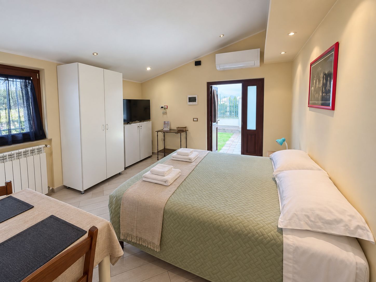 Habitación de hotel con cama, escritorio, televisión y ventana con cortinas.