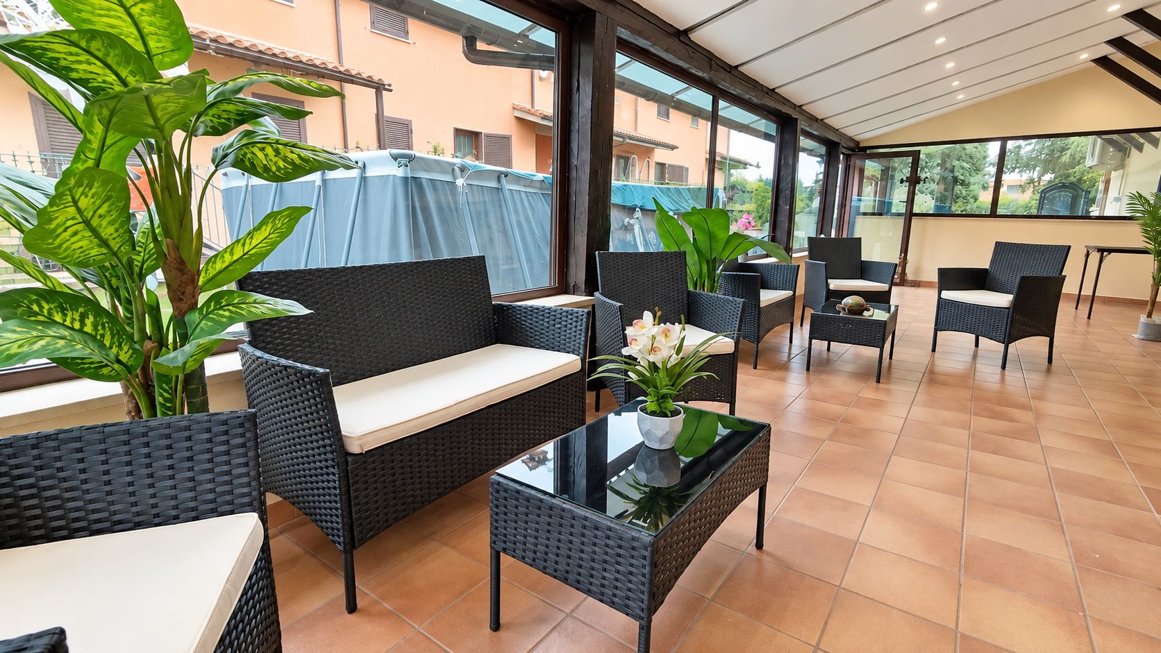 Un espace extérieur aménagé, abrité et doté de mobilier en osier et de plantes en pot.