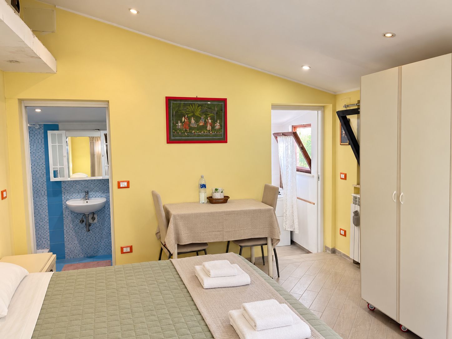 Ein Hotelzimmer mit einem Bett, einem Tisch mit Stuhl, einem Waschbecken und einem Kleiderschrank.
