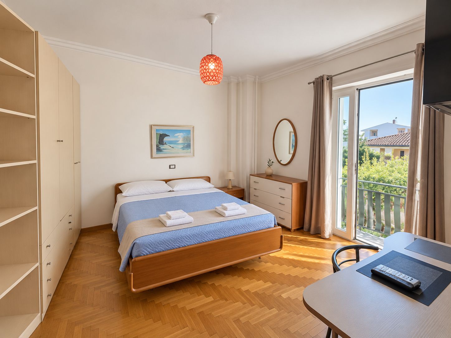 A bedroom with a bed, bedside table, dresser, and a view of the outside.