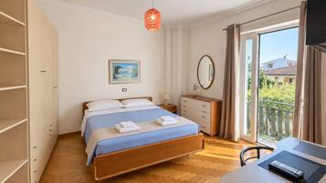 A bedroom with a bed, bedside table, dresser, and a view of the outside.