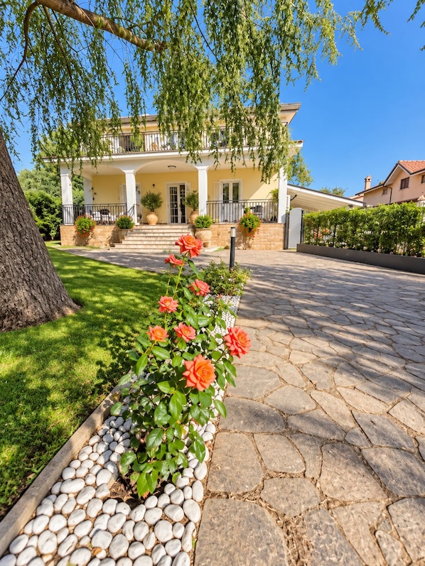 Une maison à deux étages avec un porche, un chemin de pierre et une rangée de fleurs rouges.