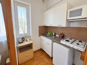 Une cuisine compacte équipée d’une cuisinière à gaz, d’un four à micro-ondes, d’un évier et d’une fenêtre avec des rideaux.