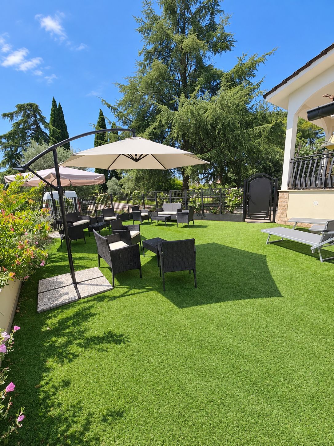 An outdoor patio area with seating and umbrellas, surrounded by greenery and trees.