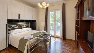 A hotel room with a bed, a desk, a chair, a television, and a balcony with curtains.