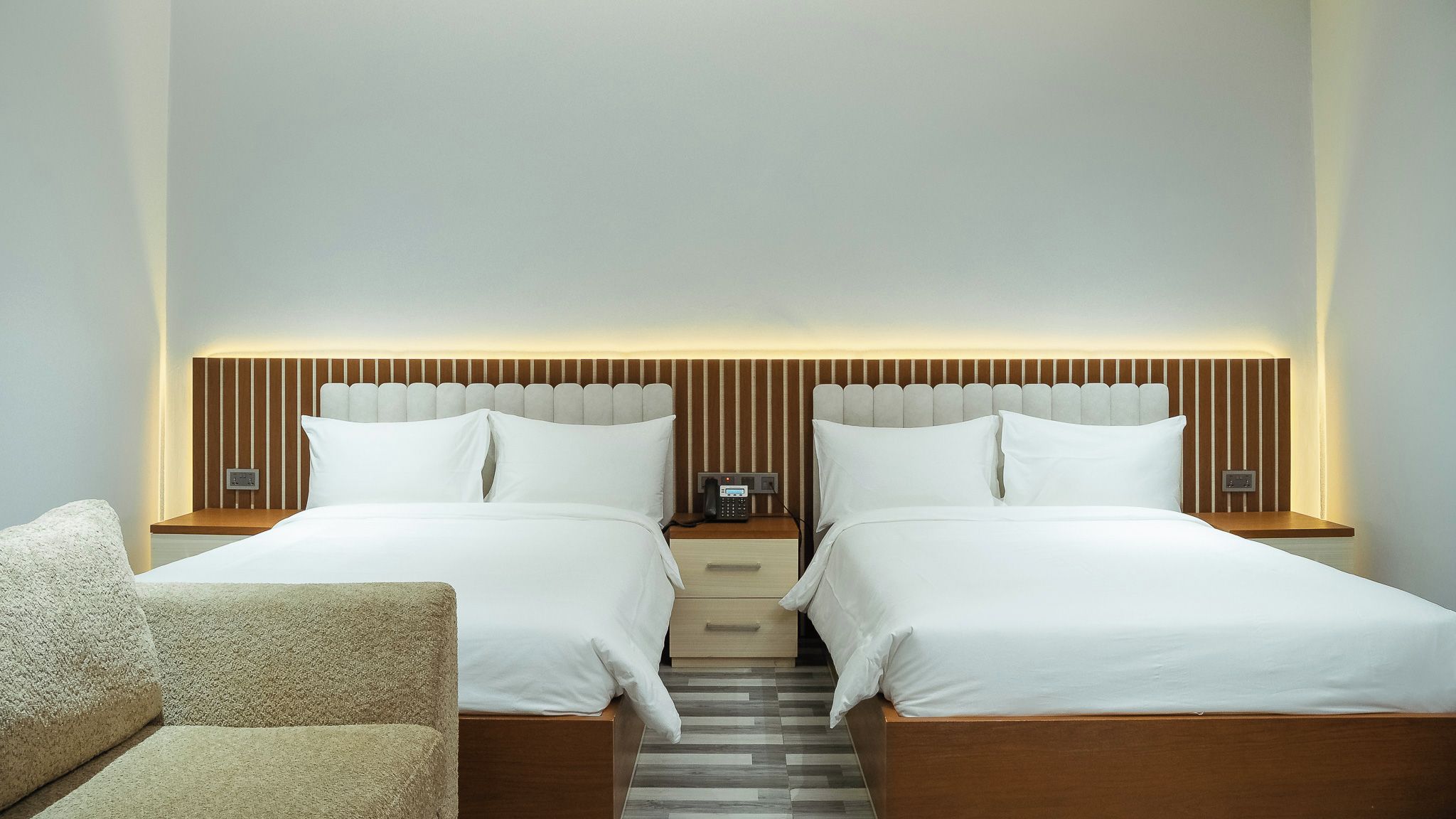A hotel room with two beds, a wooden headboard, bedside tables, a phone, and a chair.