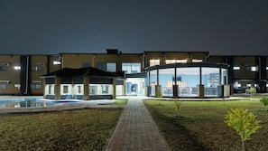 A hotel with a swimming pool, a covered outdoor seating area, and a paved walkway.