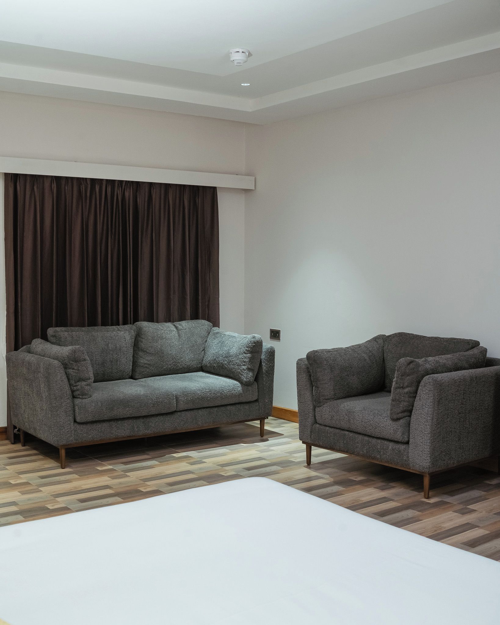 A modern living room with a grey sofa, a smaller armchair, and a patterned rug.