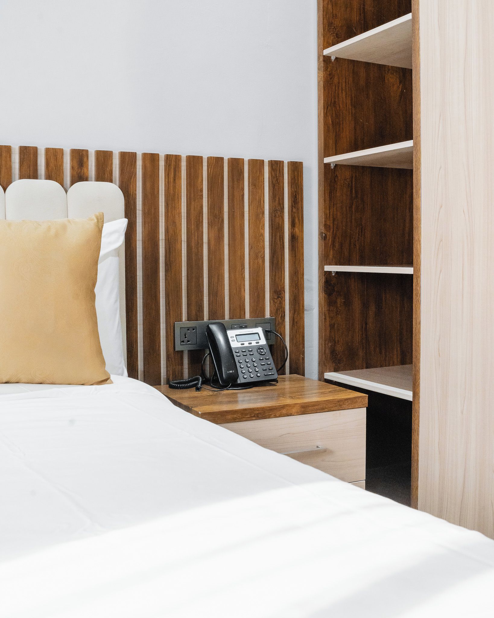 A hotel room with a bed, a bedside table with a telephone, and a wooden headboard.