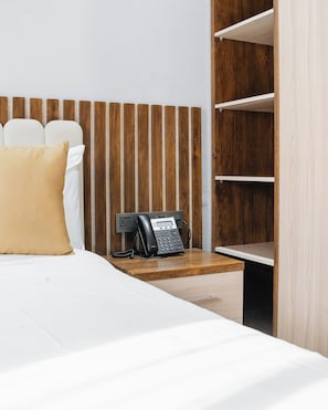 Quarto de hotel com cama, mesa de cabeceira e painel de cabeceira de madeira.
