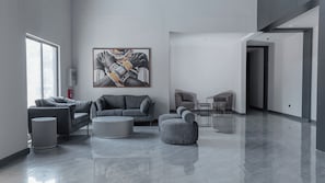 A modern living room with a grey sofa, ottoman, and armchair, a round coffee table, and a large abstract painting on the wall. - The Urban Stay Kalumbila (Kalumbila)