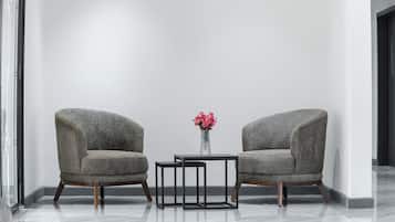 Two armchairs with wooden legs, a small table, and a vase with pink flowers in a modern room with a plain white wall and a glass door.