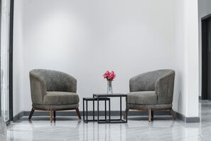 Two armchairs with wooden legs, a small table, and a vase with pink flowers in a modern room with a plain white wall and a glass door. - The Urban Stay Kalumbila (Kalumbila)