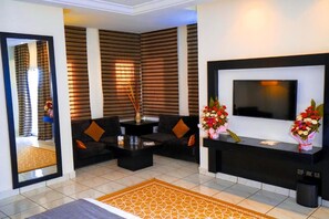 A modern living room with a sofa, coffee table, and a flat-screen TV. There are decorative vases with flowers on a console table.