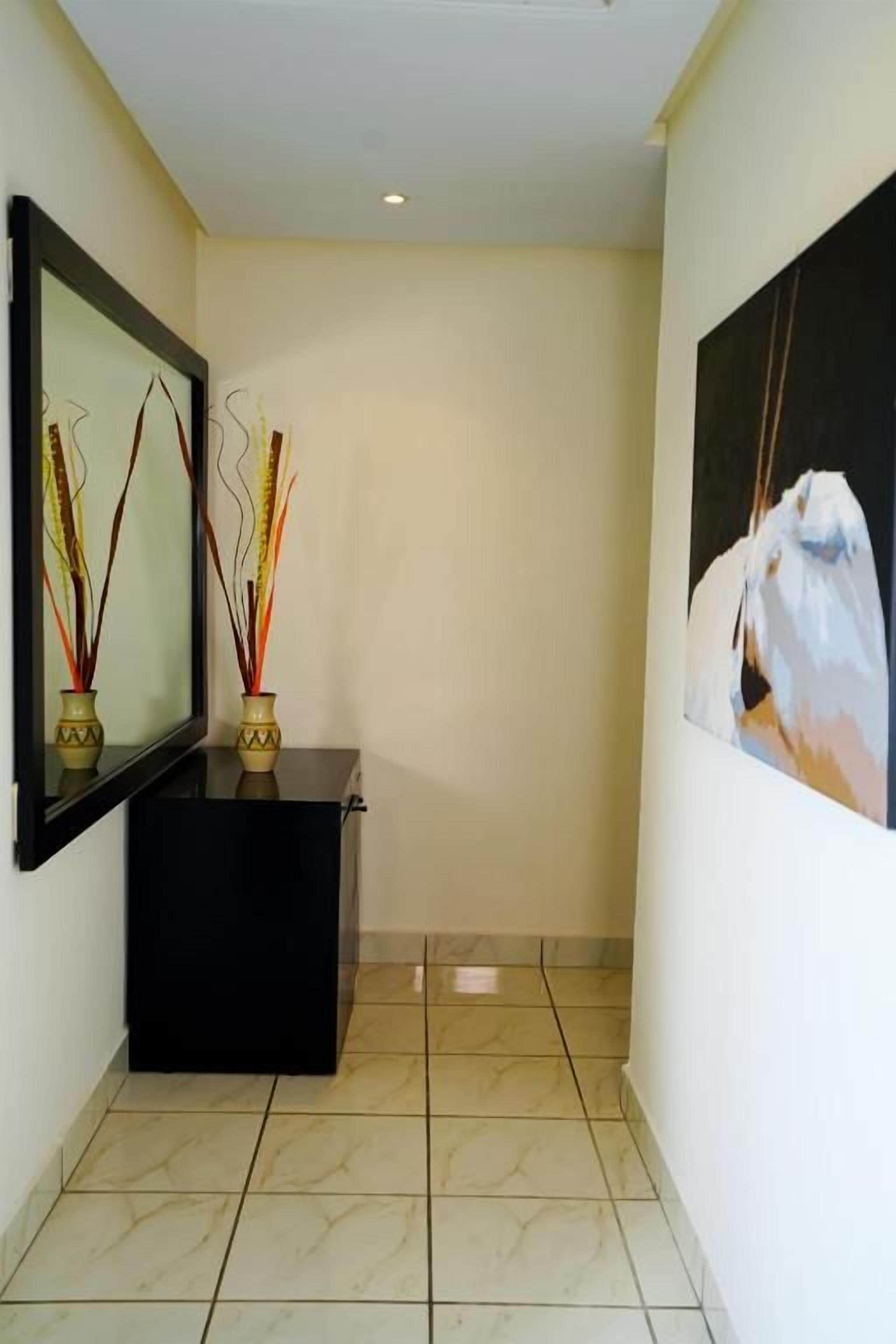 Un couloir avec une console noire, deux tableaux accrochés au mur et un sol carrelé.