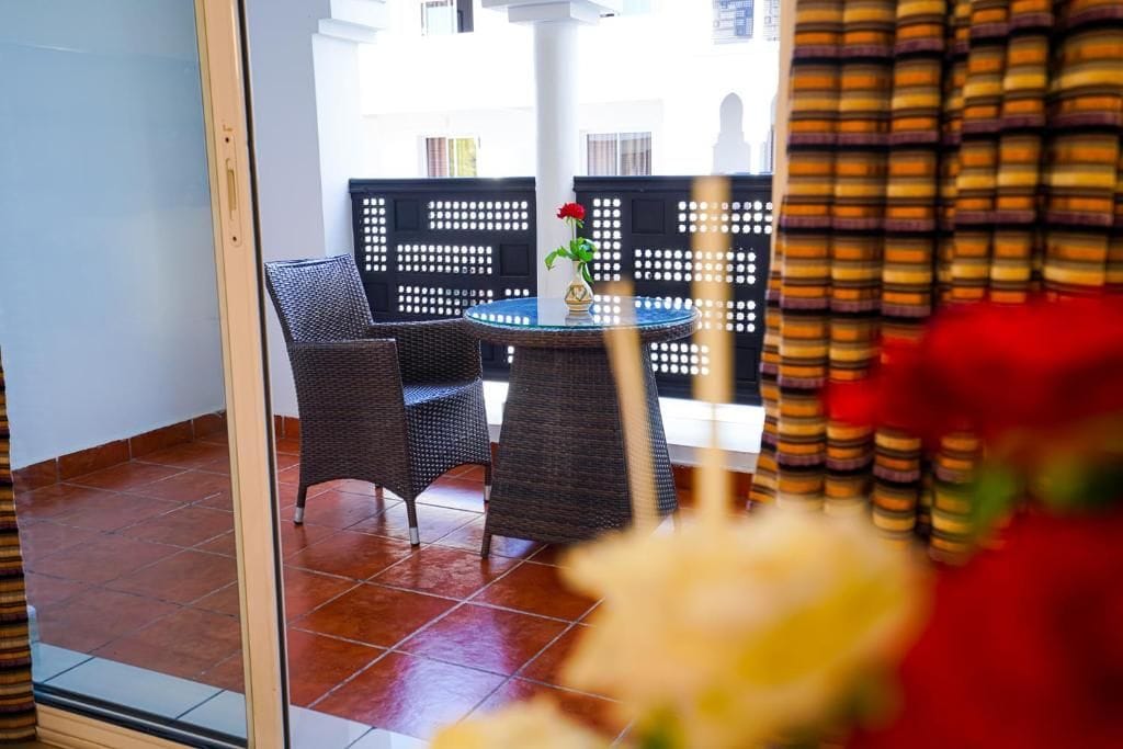 Una habitación con una mesa redonda y dos sillas, una planta en maceta y vistas a través de una puerta de cristal.