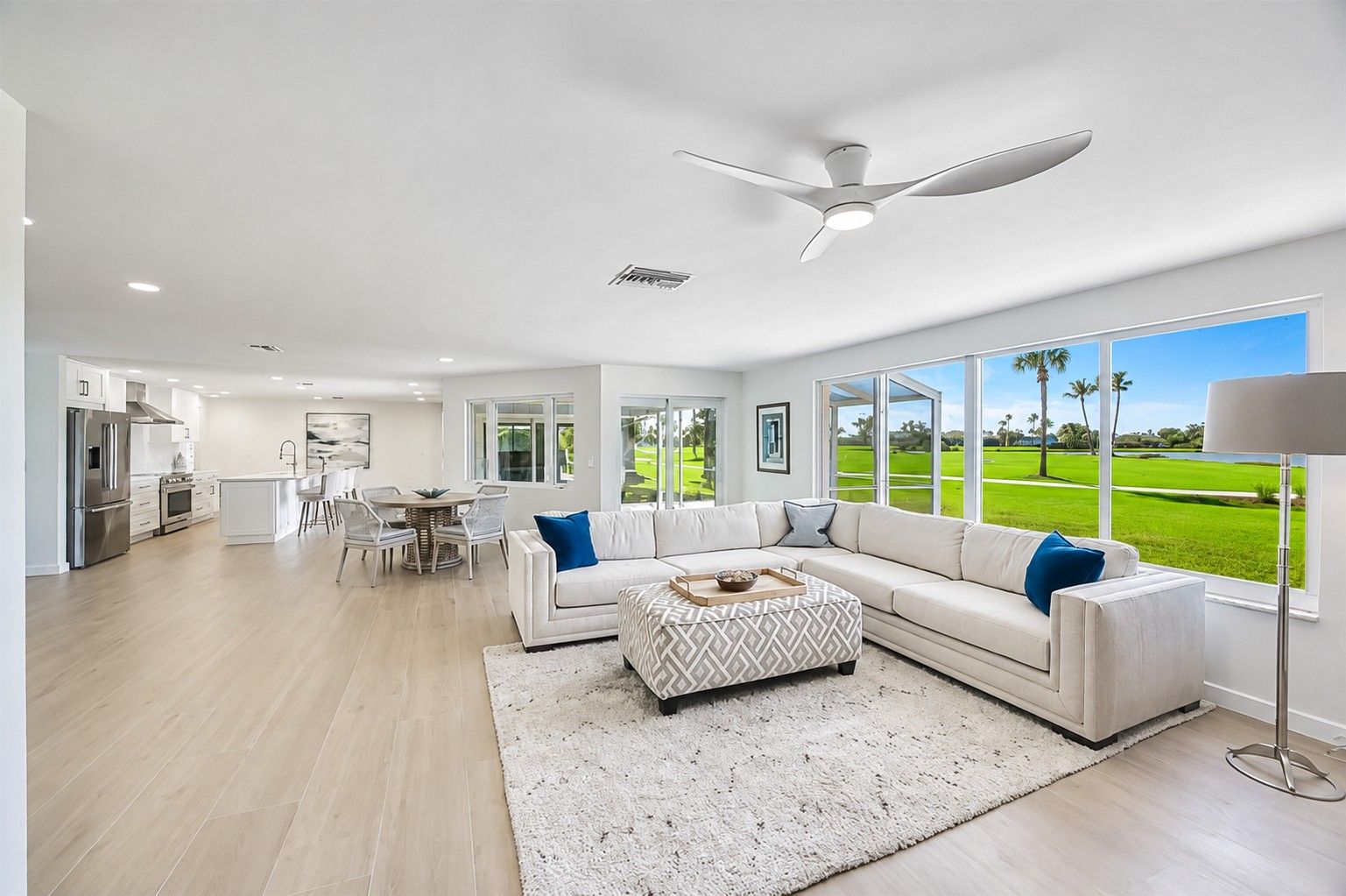 A modern living room with a large window, a ceiling fan, and a dining area with a view of a golf course.