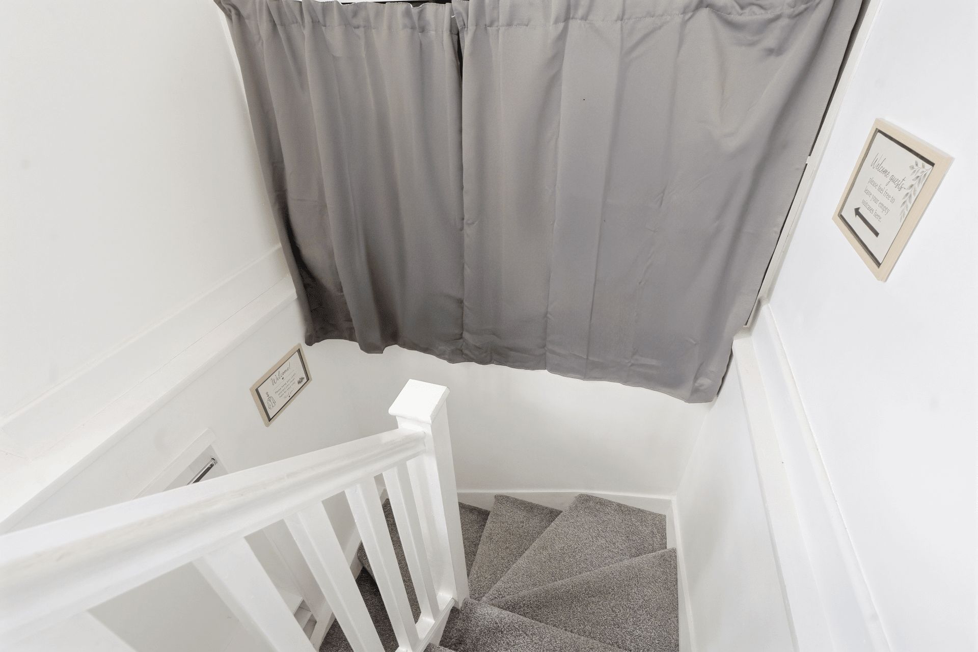 A staircase with a white railing, grey carpeted steps, and a grey curtain.