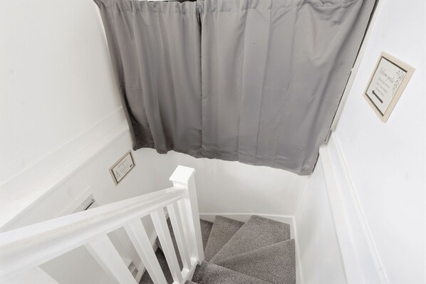 A staircase with a white railing, grey carpeted steps, and a grey curtain.