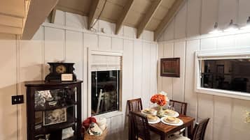 A dining area with a wooden table set for four, a chandelier, and a view through a window.