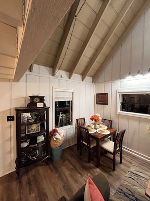 A dining area with a wooden table set for four, a chandelier, and a view through a window.