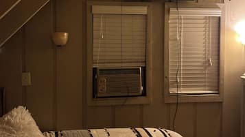 A bedroom with a bed, a television mounted on the wall, and two windows with blinds.