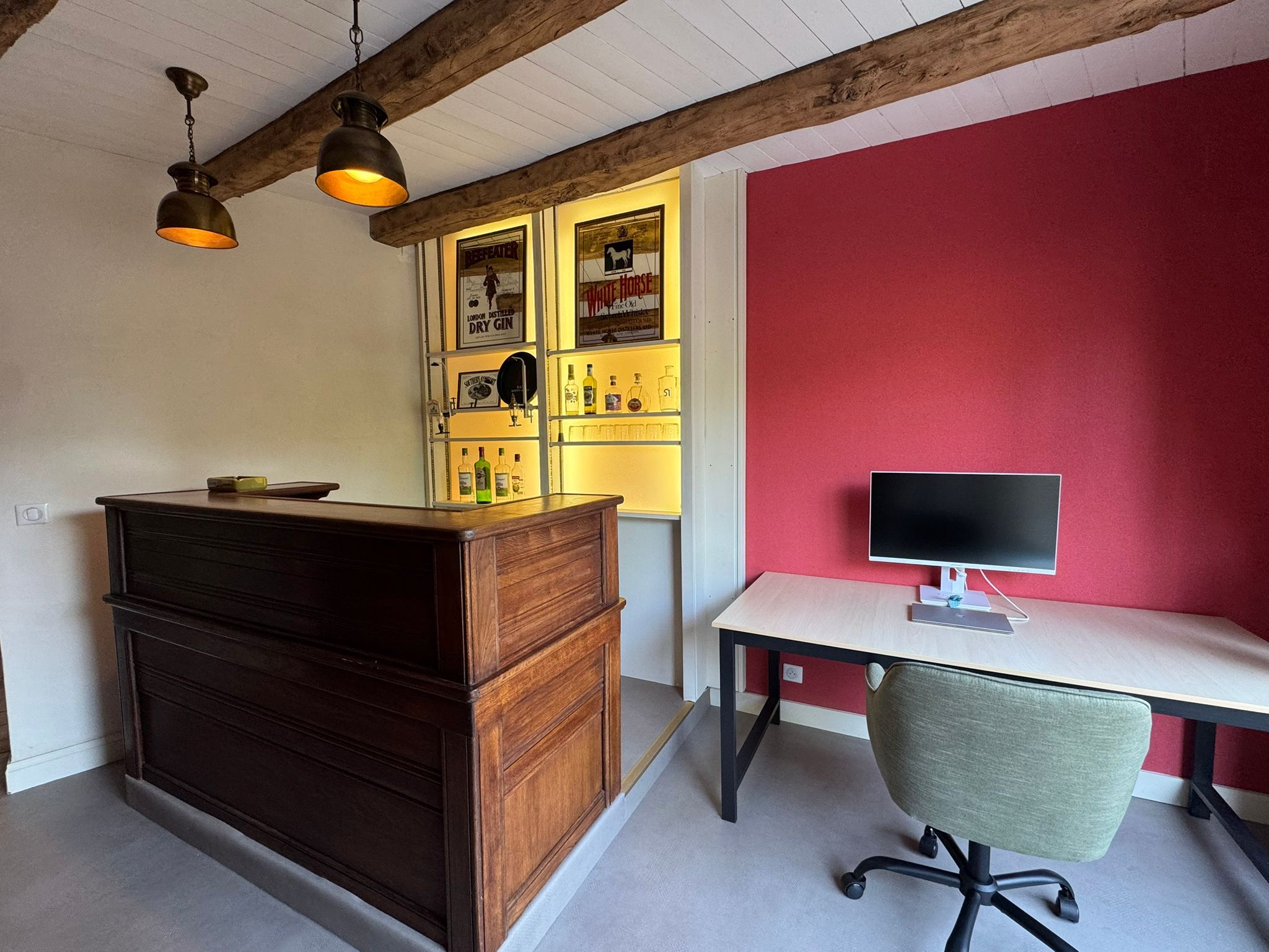 Une pièce avec un meuble en bois, un bureau avec un ordinateur et un mur d’accent de couleur rouge.