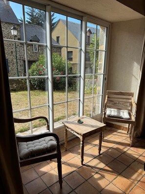 A room with a large window, a wooden table, a cushioned chair, and a bench.