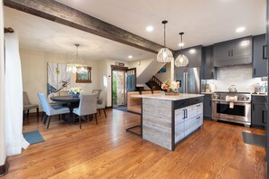 A modern kitchen with a central island, stainless steel appliances, and a dining area with a large table and chairs. - New! Riverside Townhome | Hot Tub | 3 Min to Beaver Creek (Avon)