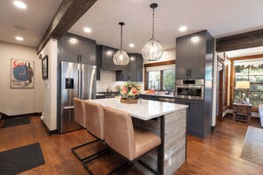 A modern kitchen with stainless steel appliances, a central island with seating, pendant lighting, and a view to the outdoors. - New! Riverside Townhome | Hot Tub | 3 Min to Beaver Creek (Avon)