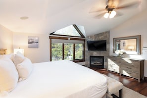 A bedroom with a large bed, a fireplace, a television, and a stone wall. - New! Riverside Townhome | Hot Tub | 3 Min to Beaver Creek (Avon)