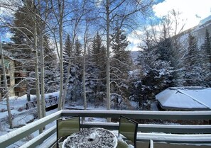 A snow-covered balcony with a table and chairs, overlooking a forested area with snow-covered trees. - New Listing! Ski-In Ski-Out Penthouse | Sauna | Hot Tub | Pool (Vail)