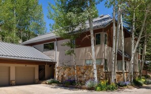 A two-story house with a stone facade, a garage, and a landscaped front yard with trees and shrubs. - New Listing! Ski-In Ski-Out Penthouse | Sauna | Hot Tub | Pool (Vail)