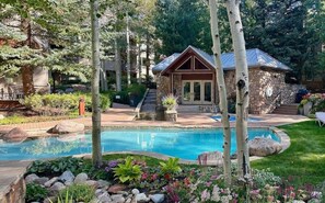 A pool area with a stone building, surrounded by trees and a well-maintained garden. - New Listing! Ski-In Ski-Out Penthouse | Sauna | Hot Tub | Pool (Vail)