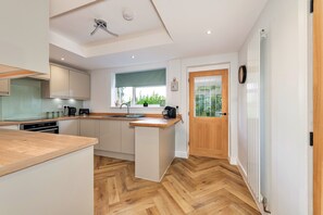 A modern kitchen with a wooden countertop, built-in appliances, and a window with a view of greenery. - Mill House, Staffordshire (Stafford)