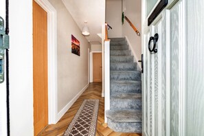 A hallway with a wooden door, a grey carpeted staircase, and a patterned rug. - Mill House, Staffordshire (Stafford)