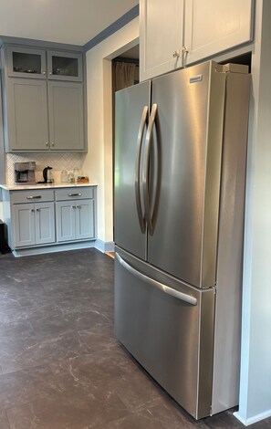 A kitchen with a stainless steel refrigerator, grey cabinets, and a coffee maker on the countertop.