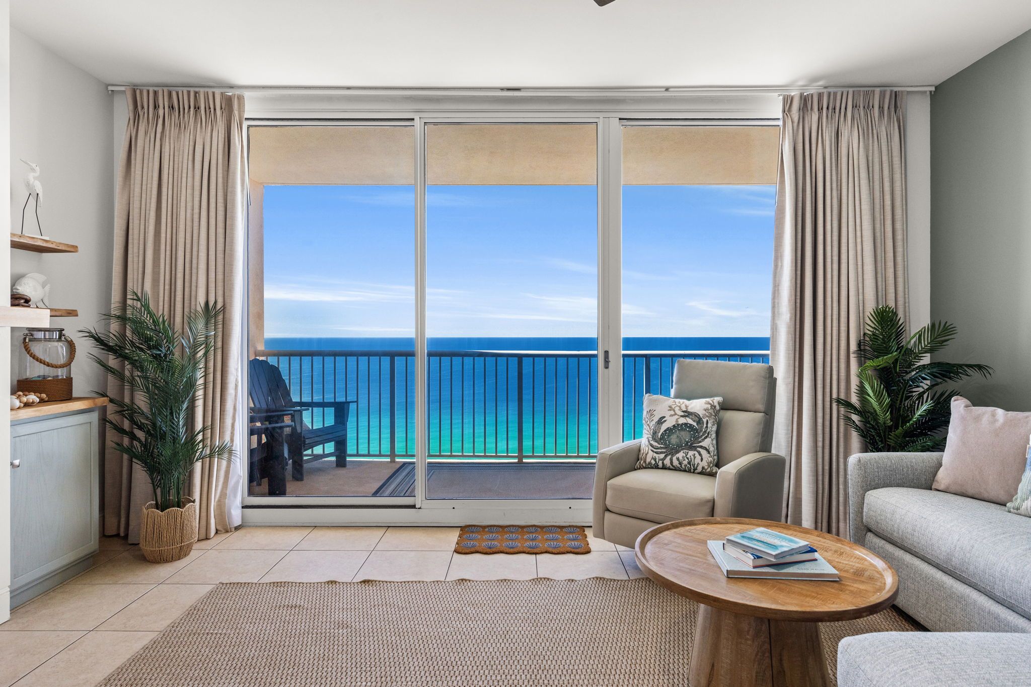 Ein modernes Wohnzimmer mit Balkon und Meerblick, ausgestattet mit einer Couch, einem Sessel, einem Couchtisch und einem Essbereich.