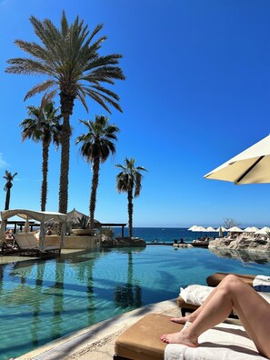 A poolside area with lounge chairs, umbrellas, and palm trees. - LUXURY TWO BEDROOM PRESIDENTIAL SUITE at Grand Solmar Land’s End Cabo San Lucas (Cabo San Lucas)