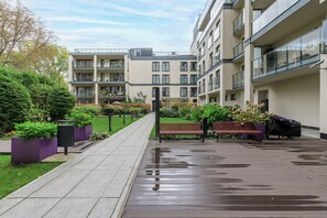 Un immeuble résidentiel doté de nombreux balcons, d’une allée pavée et d’un espace jardin agrémenté de bancs.