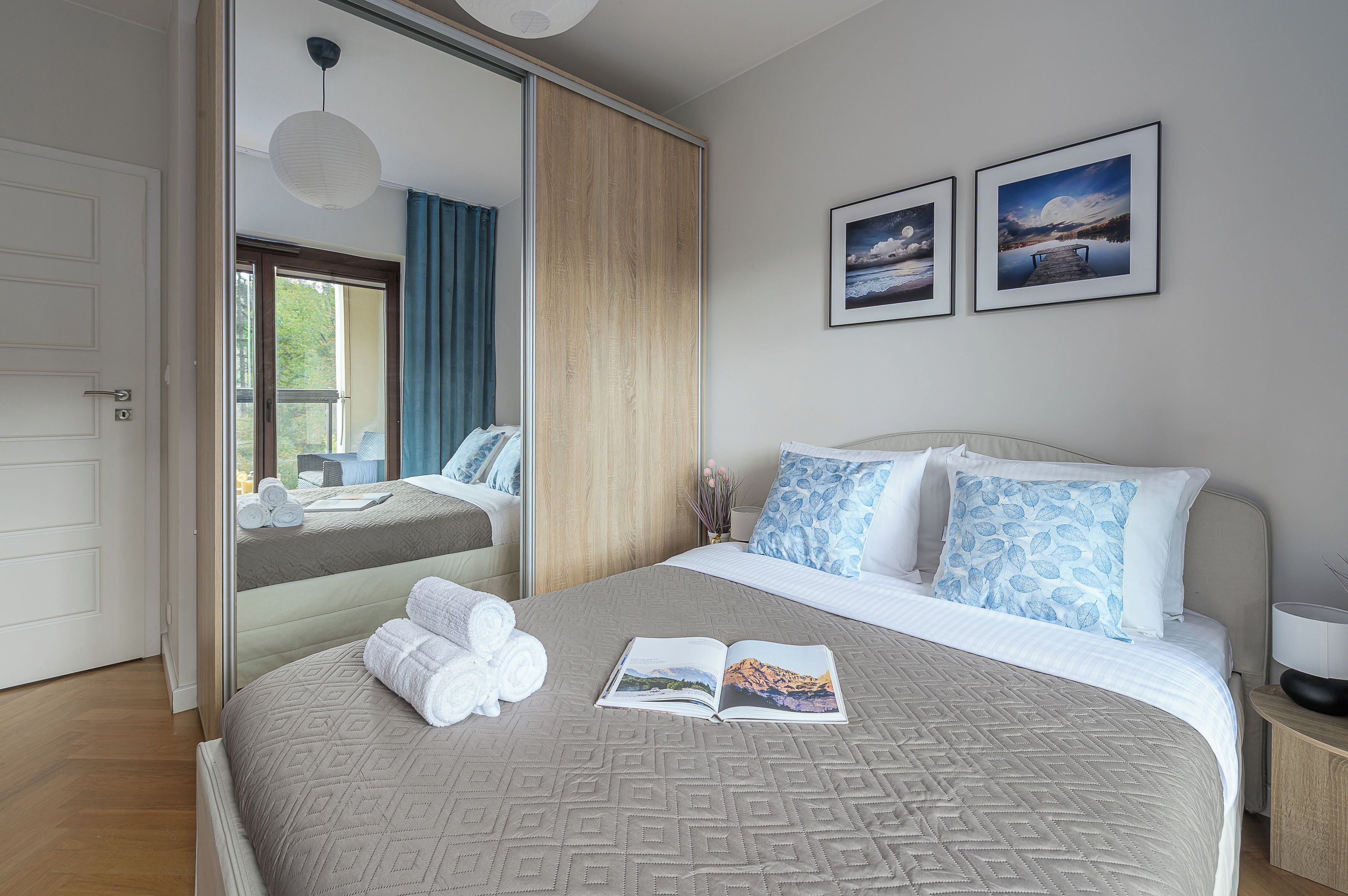 Een hotelkamer met een bed, een grote spiegel, een raam met gordijnen en twee ingelijste foto's aan de muur.