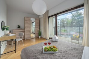 Moderni hotellihuone, jossa on suuri sänky, työpöytä, tuoli, vaatekaappi ja parveke, jolta on näkymä kaupunkiin.