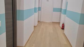 Un couloir avec un plancher en bois, des murs blancs à rayures bleues et un extincteur sur le côté droit.