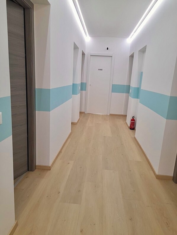 A hallway with wooden flooring, white walls with blue stripes, and a fire extinguisher on the right. - Vrbo Property (Olbia)