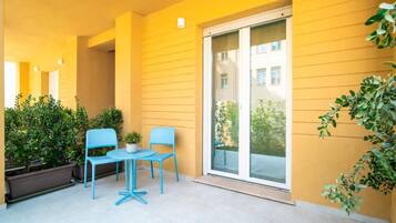 Un balcon avec un revêtement jaune, une porte-fenêtre coulissante et deux chaises bleues.