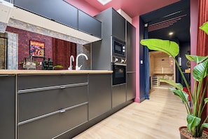 A modern kitchen with dark cabinetry, a stainless steel sink, and a large potted plant. - Vrbo Property (Armentières)