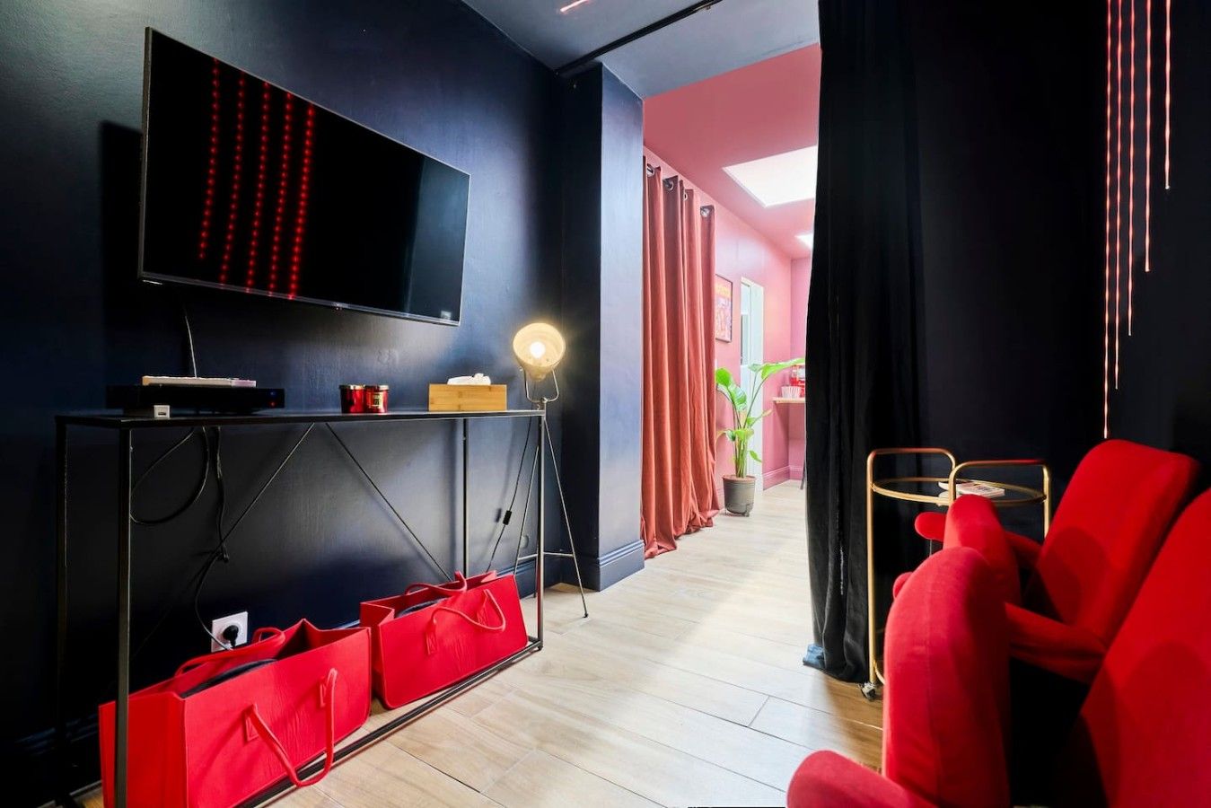 Ein modernes Wohnzimmer mit Flachbildfernseher, einem roten Sofa, einem kleinen Tisch und einer Topfpflanze.