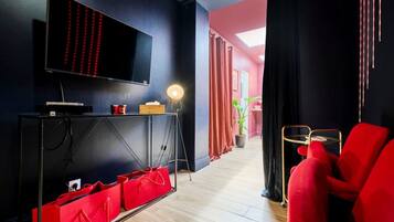 Ein modernes Wohnzimmer mit Flachbildfernseher, einem roten Sofa, einem kleinen Tisch und einer Topfpflanze.