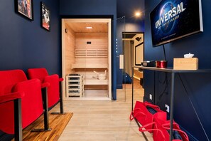 A room with a wooden sauna, red seating, a television, and a wooden cabinet with items on top.